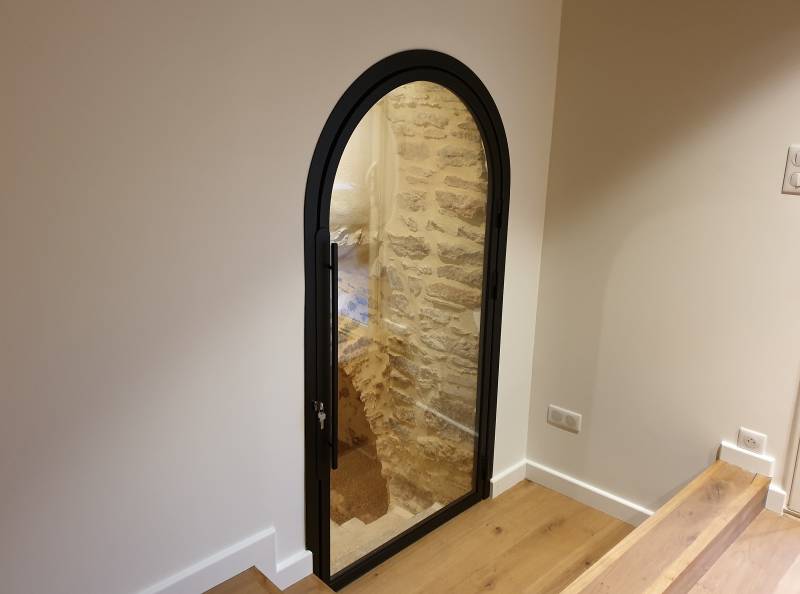 Porte originale en acier verre, voutée, pour un accès inférieur dans la commune de Saint Julien