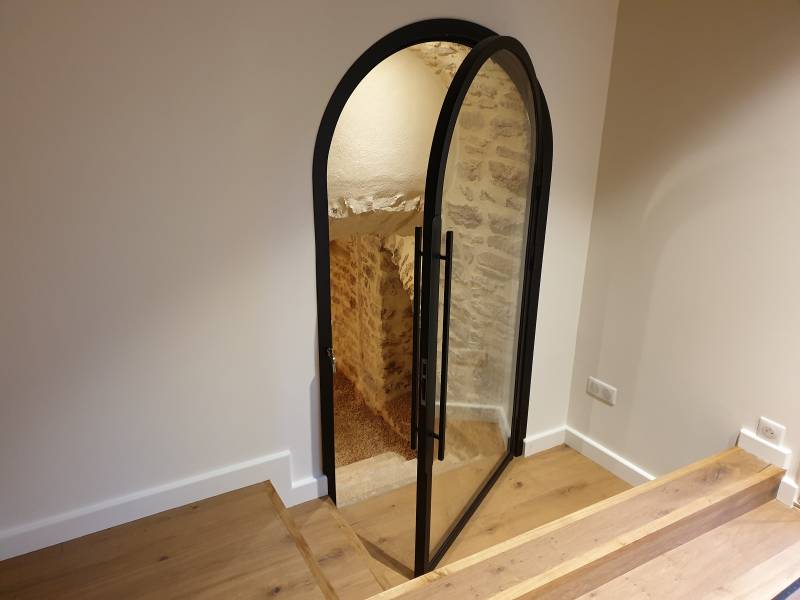 Porte originale en acier verre, voutée, pour un accès inférieur dans la commune de Saint Julien