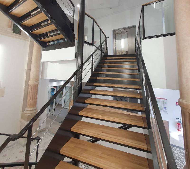 Escalier intérieur en acier avec double quart tournant, paliers sécurisés et garde-corps vitrés, conçu sur mesure pour un bâtiment ERP accessible aux personnes en situation de handicap.