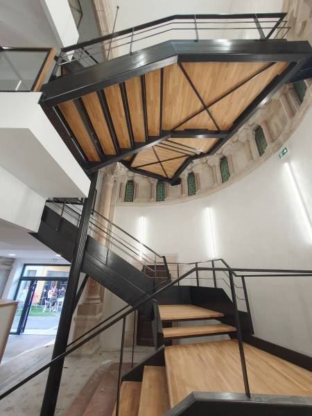 Vue d’ensemble de l’escalier double quart tournant en acier, intégrant deux paliers et des marches bois antidérapantes dans un bâtiment réhabilité du Haut Beaujolais.