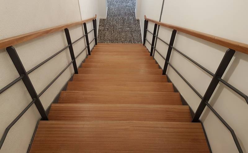 Escalier large entre deux cloisons, marches vissées par-dessous et contre-marches acier, pour desservir zone de bureau fonctionnelle.